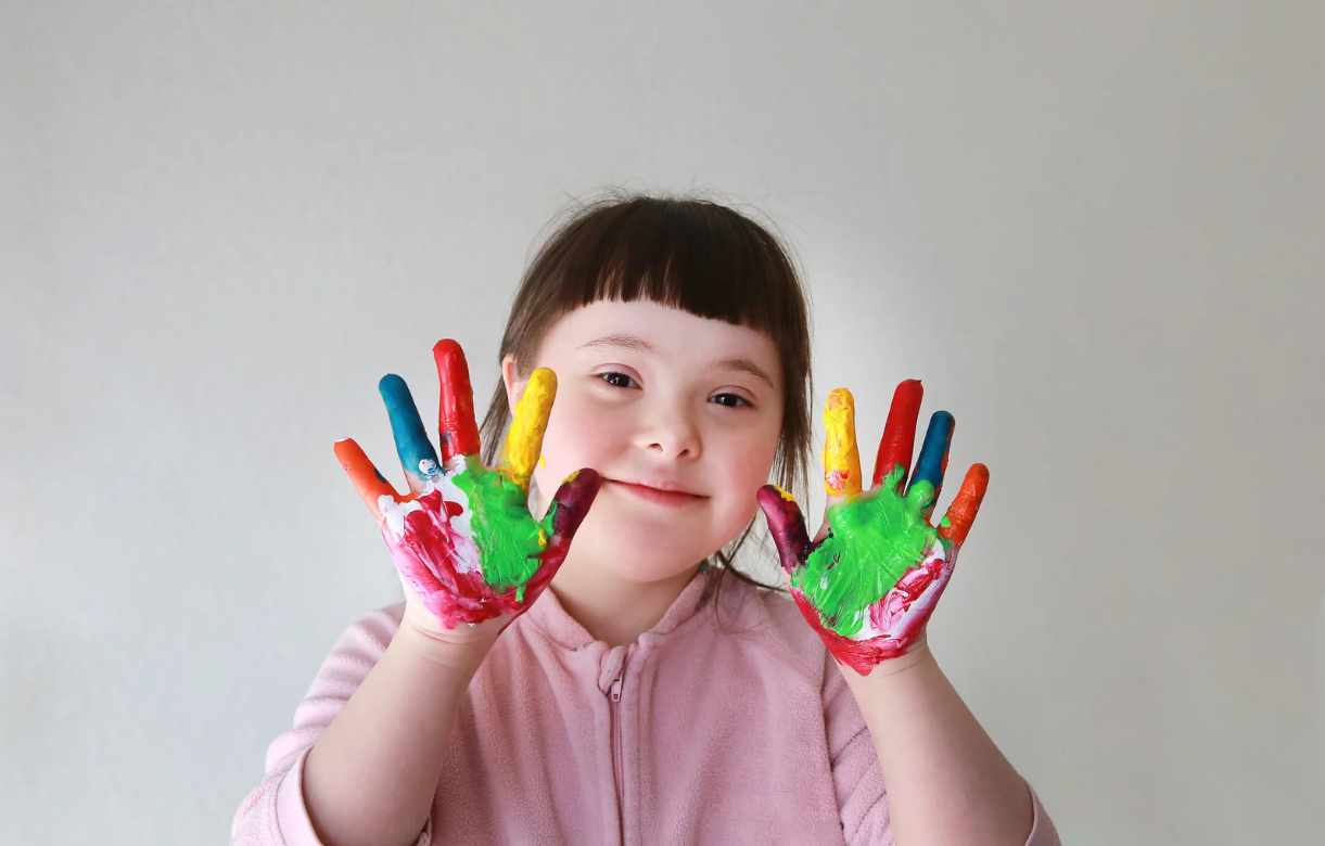 child with special needs smiling and showing painted hands at pediatric dental office in Bedminster