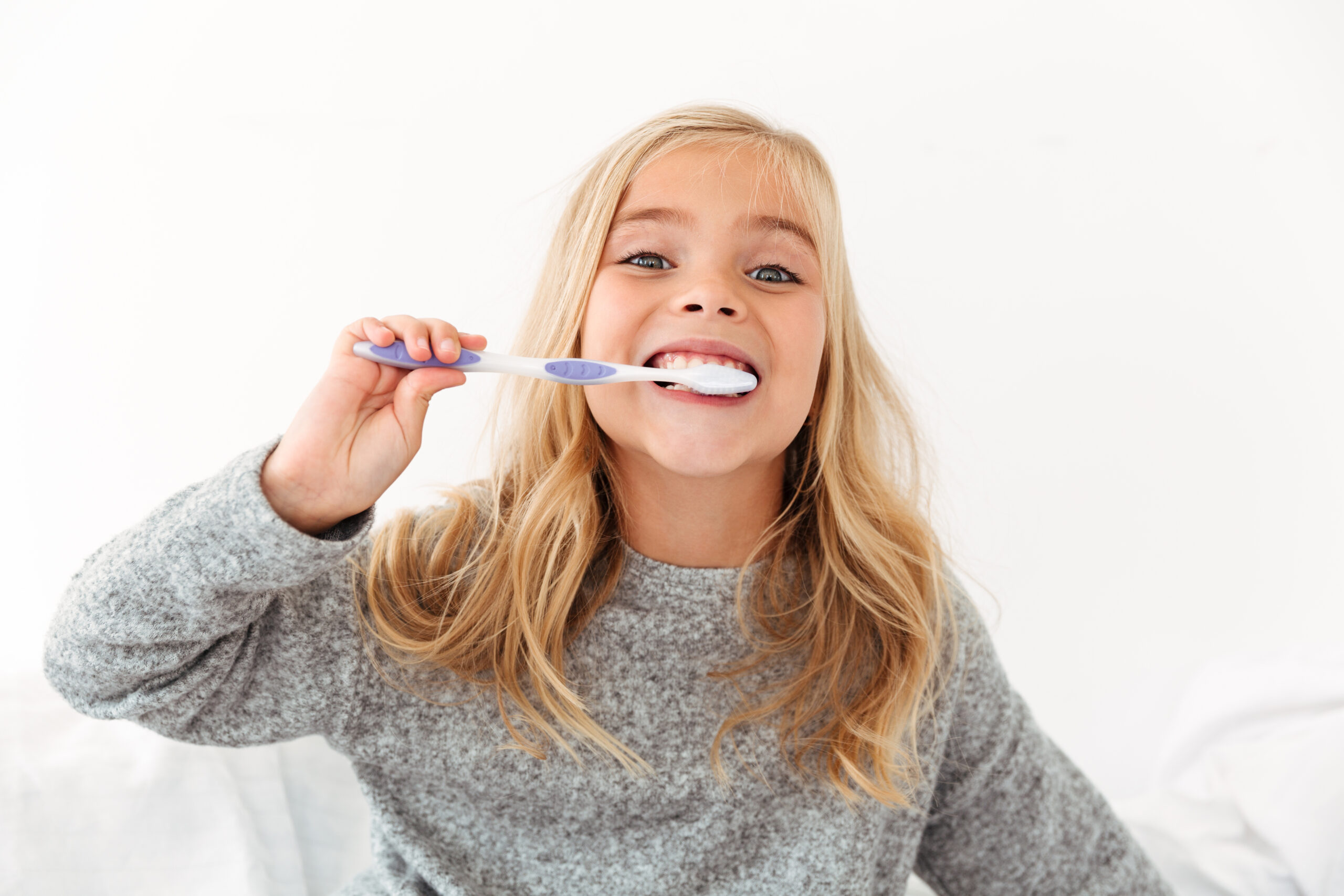 Close-up portrait of cute kid in gray pajamas brushing her teeth